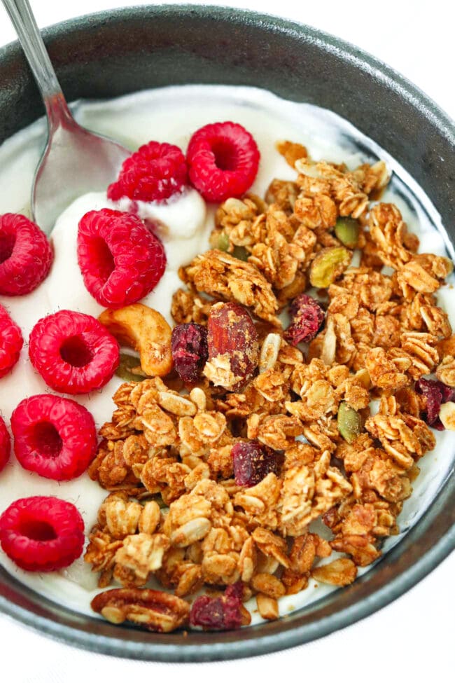 Closeup of bowl with Greek yogurt, peanut butter granola, raspberries and a spoon.
