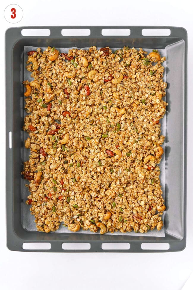 Unbaked granola mixture spread flat on a nonstick paper lined baking tray.