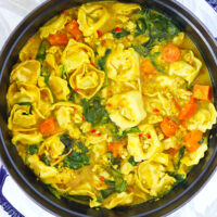 Curry tortellini soup in a Dutch oven. Text overlay "Thai Yellow Curry Tortellini Soup" and "thatspicychick.com".