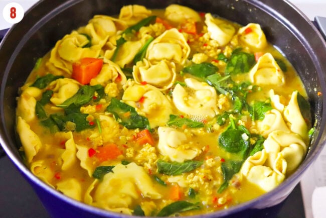 Added baby spinach and Thai sweet basil to yellow curry tortellini soup in pot.