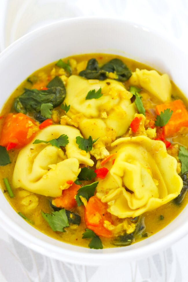 Closeup front view of bowl with yellow curry tortellini soup.