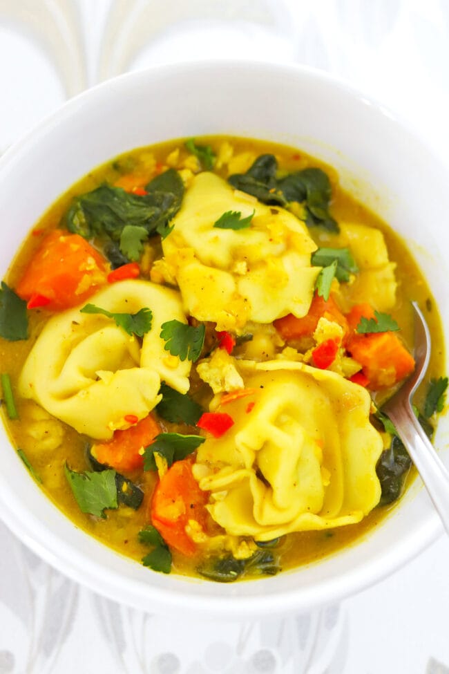 Front view of bowl with yellow curry tortellini soup and a spoon.