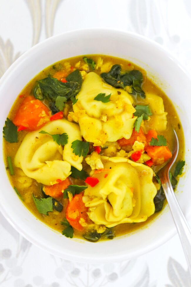 Top view of bowl with yellow curry tortellini soup and a spoon.