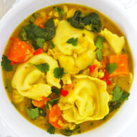 Curry tortellini soup in a bowl. Text overlay "Thai Yellow Curry Tortellini Soup" and "thatspicychick.com".