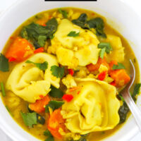 Curry tortellini soup in a bowl with a spoon. Text overlay "Thai Yellow Curry Tortellini Soup" and "thatspicychick.com".