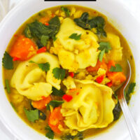 Cowl with curry tortellini soup and a spoon. Text overlay "Thai Yellow Curry Tortellini Soup" and "thatspicychick.com".