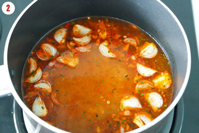Shallots, garlic and chilies simmering in broth in a pot.