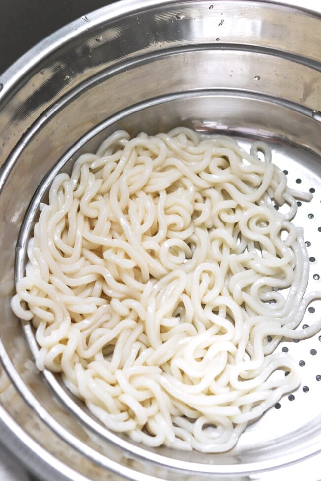 Cooked thick white noodles in a colander.