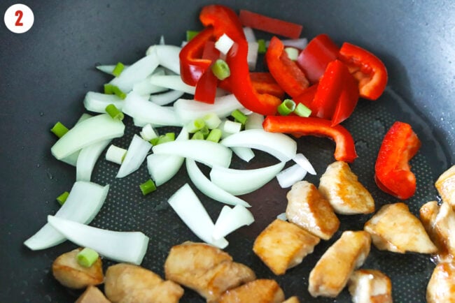 Added onion, spring onion and red bell pepper to wok with cooked chicken pieces.
