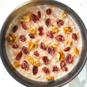 Bowl with carrot cake overnight oats topped with chopped walnuts and dried cranberries.