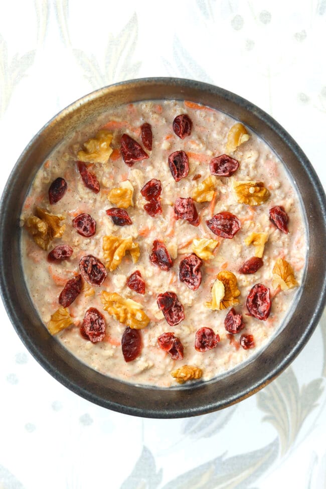 Bowl with carrot cake overnight oats topped with chopped walnuts and dried cranberries.