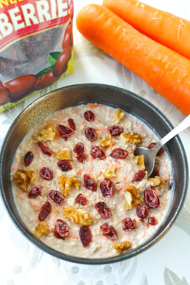 Spoon in bowl with carrot cake overnight oats topped walnuts and dried cranberries.