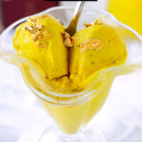 Closeup of ice cream scoops in ice cream dish with spoon. Text overlay "Golden Milk Ice Cream Ninja Creami" and "thatspicychick.com".