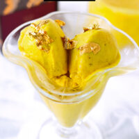 Closeup of yellow ice cream scoops in ice cream dish. Text overlay "Golden Milk Ice Cream Ninja Creami" and "thatspicychick.com".