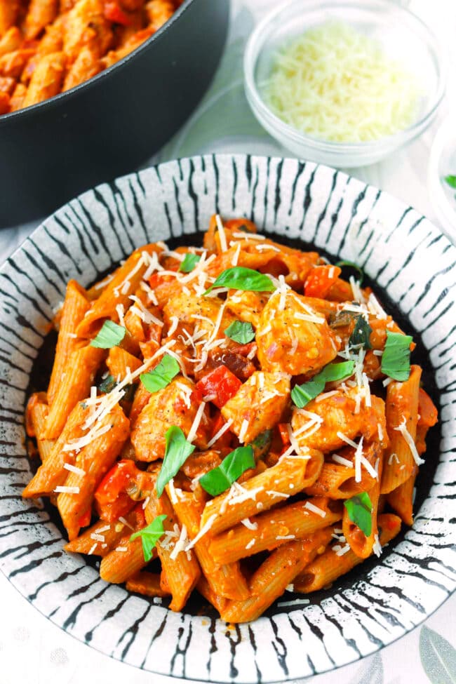 Front view of Spicy Chicken and Bacon Tomato Pasta garnished on plate and in a pan.