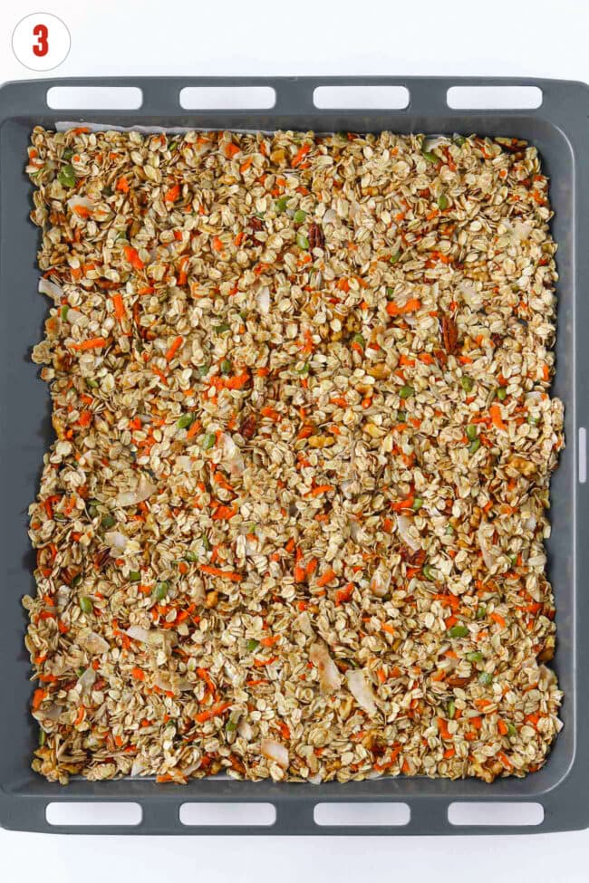 Carrot granola mixture spread out on a parchment paper lined baking sheet.