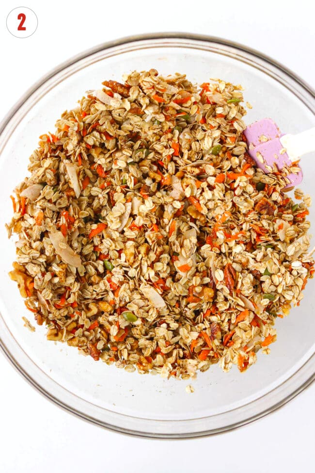 Carrot granola mixture combined with wet ingredients in a bowl with a spatula.