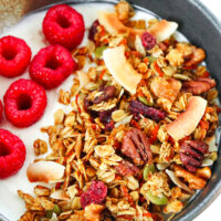 Close-up front view of homemade granola over yogurt in a bowl with raspberries. Text overlay "Carrot Cake Granola", "Healthy | Gluten-free | Vegan" and "thatspicychick.com"