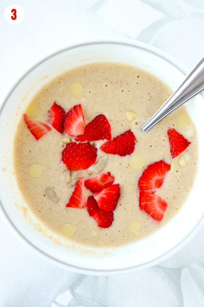 Baked oats batter in bowl with strawberries, white chocolate chips and sunflower seeds.