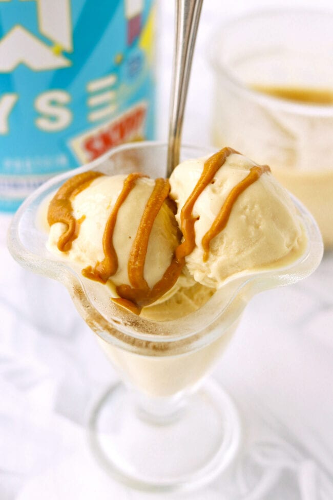 Ninja creami protein peanut butter ice cream in a glass bowl with a spoon topped with peanut butter drizzle.