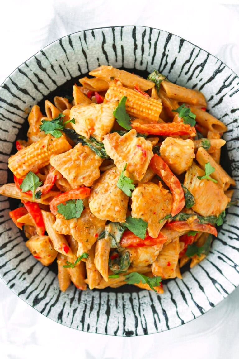 Closeup of red curry pasta with chicken garnished with cilantro on a plate.