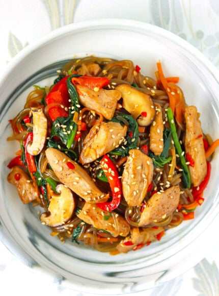 Korean japchae with chicken, carrots, mushrooms, spinach and bell pepper on a plate.