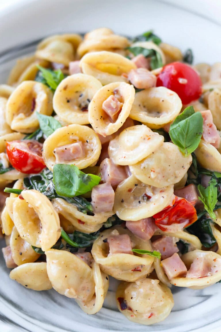 Closeup of creamy pasta with bacon and spinach on a plate.