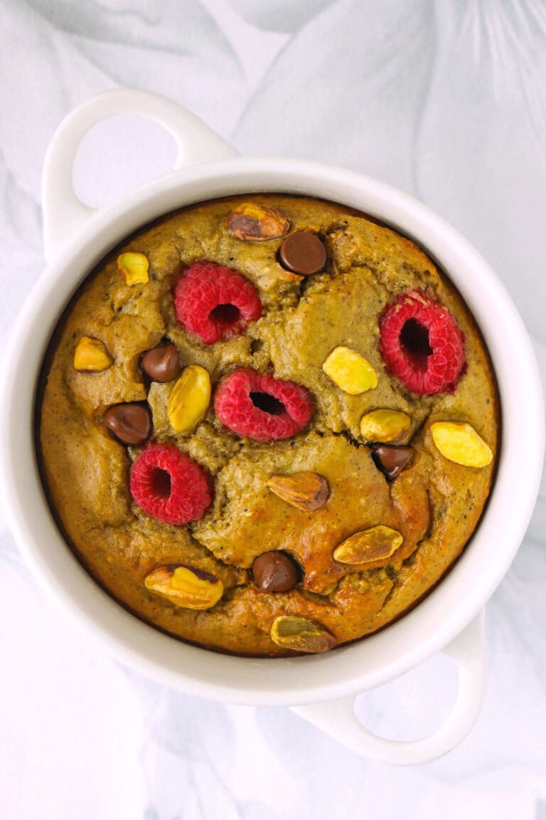 Matcha baked oats with chocolate chips, pistachios and raspberries in a white ramekin.