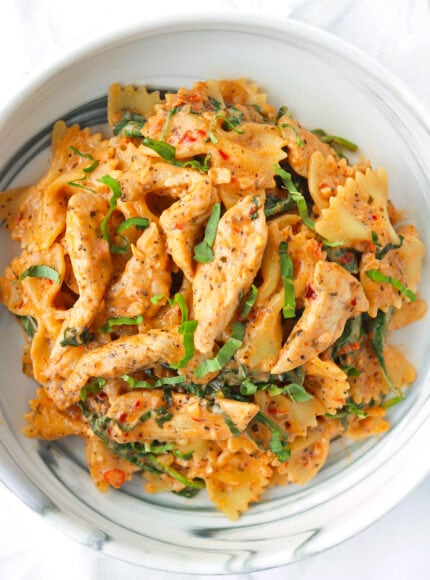 Closeup of plate with red pesto chicken pasta garnished with fresh basil.