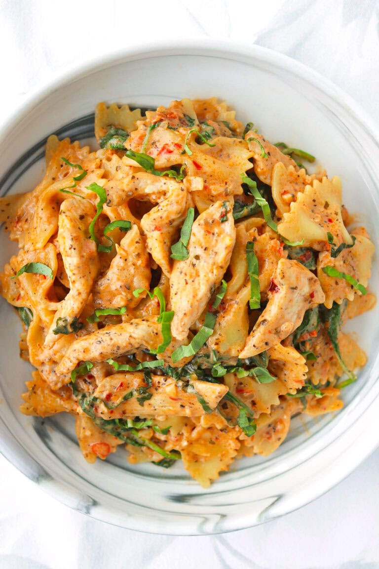 Closeup of plate with red pesto chicken pasta garnished with fresh basil.