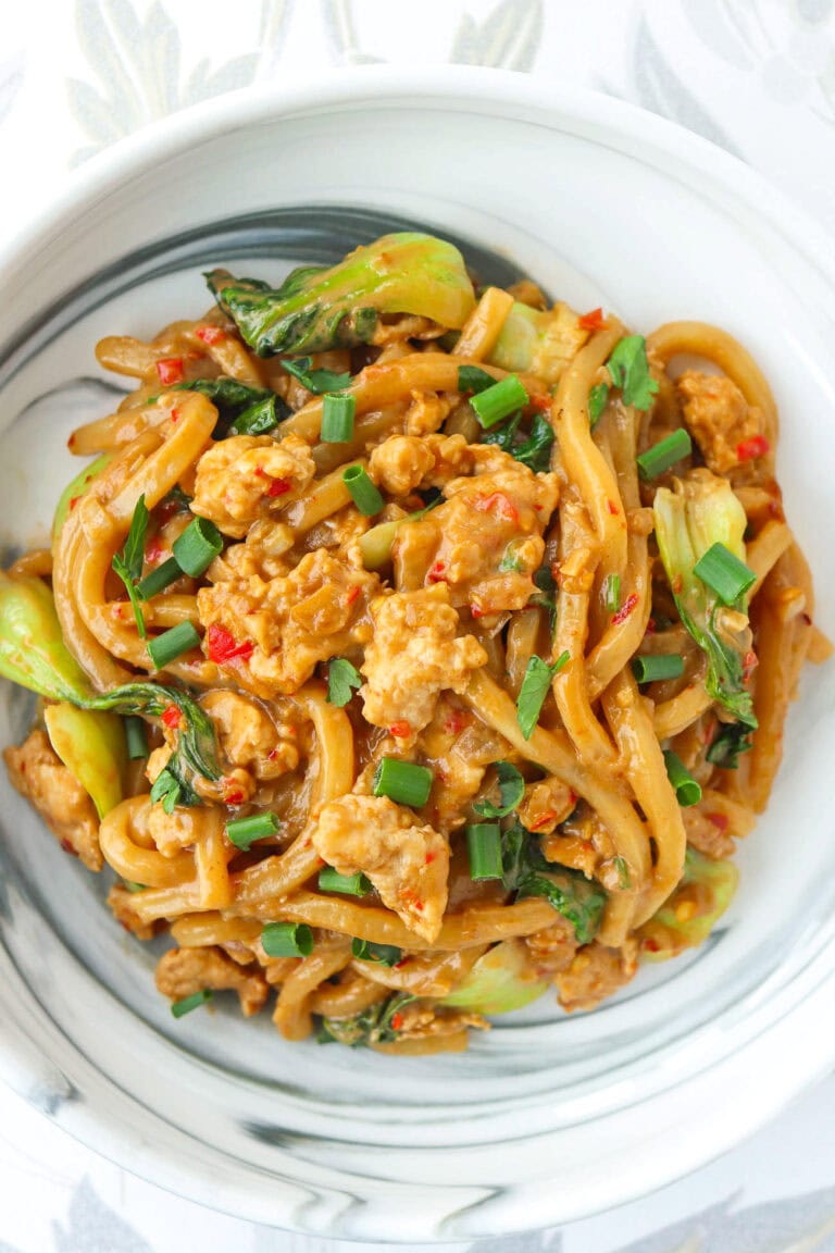 Closeup top view of plate with spicy peanut butter noodles with chicken garnished with green onions and cilantro.