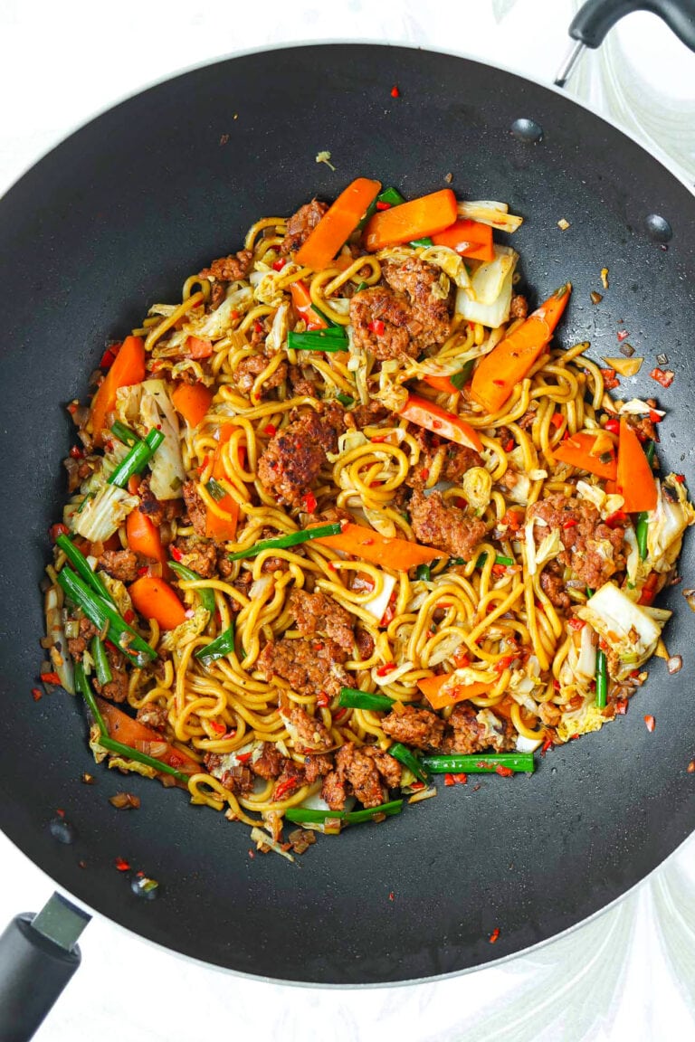 Stir-fried noodles with vegetables and char siu ground meat in a black wok.