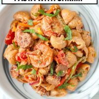 Closeup of plate with creamy shrimp and sausage pasta. Text overlay "Creamy Cajun Sausage Pasta with Shrimp" and "That Spicy Chick".