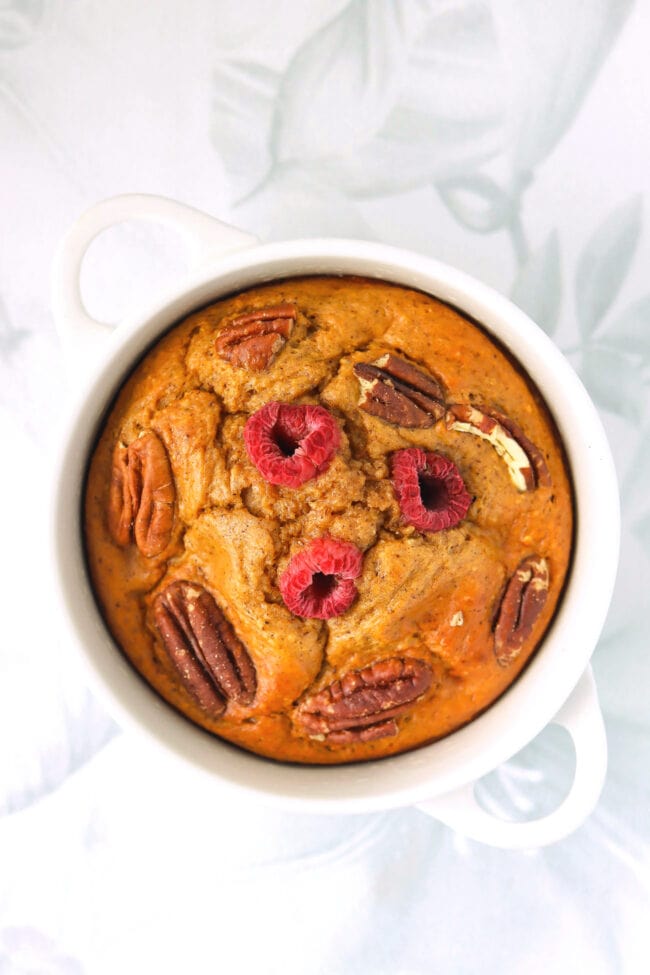 Healthy gingerbread baked oats in a ramekin with raspberries and pecans.