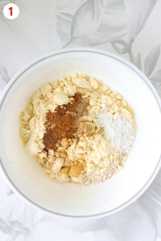 Oat flour, vanilla protein powder, warm spices and baking powder in a bowl.