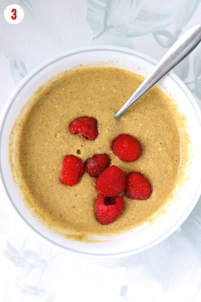 Added fresh raspberries to gingerbread oatmeal batter in a bowl with a spoon.