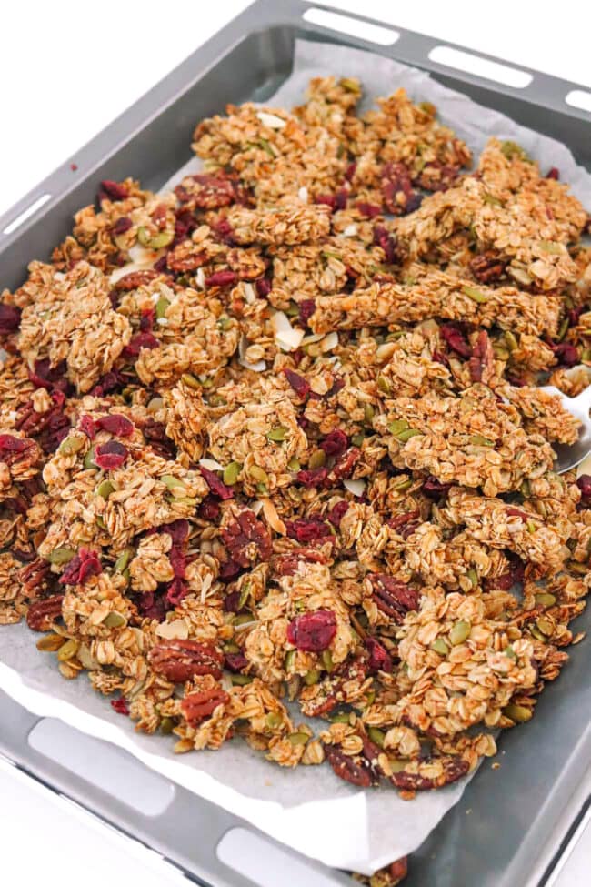 Pecan pie granola with coconut flakes and dried cranberries on a baking tray.