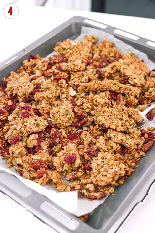 Dried cranberries stirred through pecan pie granola on a parchment paper lined baking tray.
