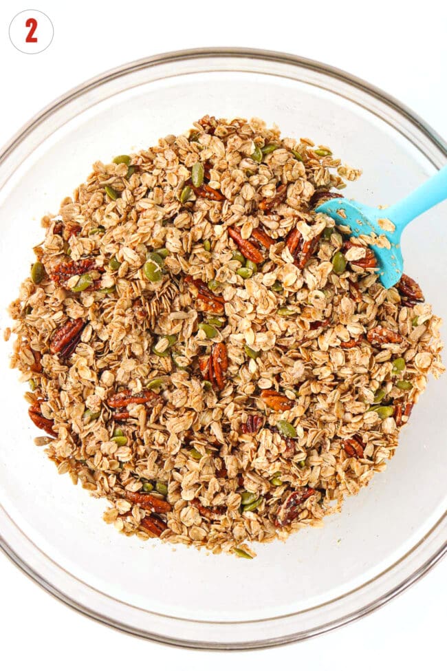 Pecan pie granola mixture combined with maple syrup and olive oil in a large mixing bowl.