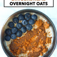 Bowl of overnight oats topped with a crumbled cookie, pecan butter, and blueberries. Text overlay "Easy " Healthy | 32G Protein", "Gingerbread Overnight Oats" and "That Spicy Chick".