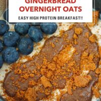 Closeup front view of bowl with overnight oats topped with blueberries, nut butter and a crumbled Biscoff cookie. Text overlay "Gingerbread Overnight Oats", "Easy High Protein Breakfast!!" and "That Spicy Chick".