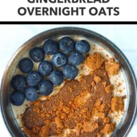 Bowl with overnight oats topped with crumbled cookie, pecan butter, and blueberries. Text overlay "Healthy Holiday Breakfast!", "Gingerbread Overnight Oats" and "That Spicy Chick".