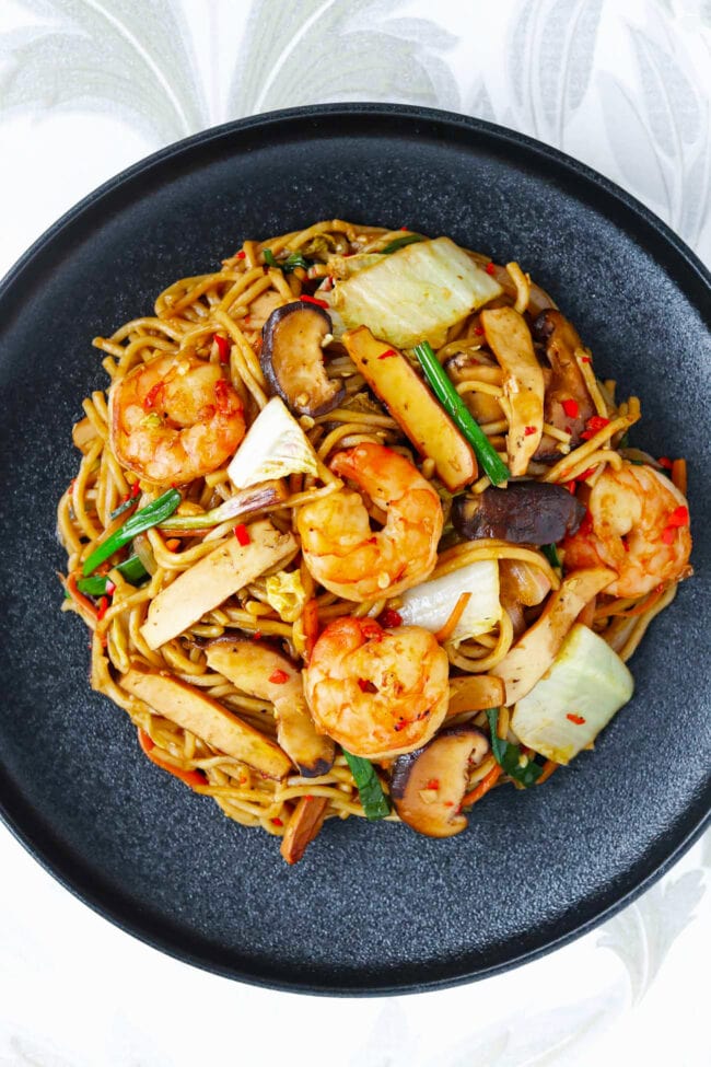 Top view of shrimp yakisoba with tofu on a a black plate.