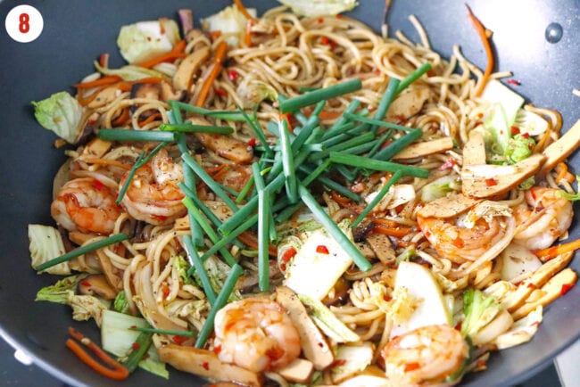 Spring onion batons in a wok with stir-fried yakisoba noodles with shrimp and tofu.
