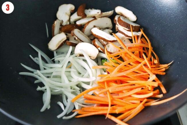 Sliced onions, carrots and mushrooms in wok.