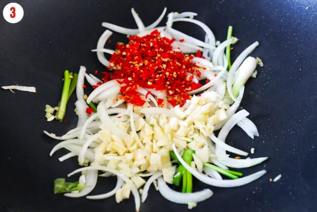 Stir-fried yellow onion, green onions, ginger, garlic, and chilies in a wok.