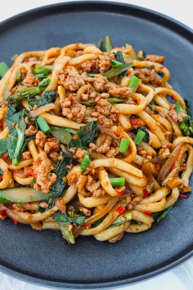 Closeup front view of spicy ground pork and Chinese broccoli udon noodles on a plate.