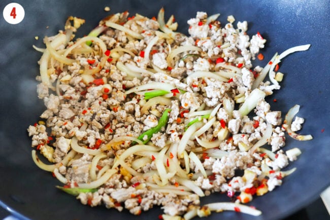 Stir-fried ground pork, onions, garlic, ginger and red chilies in a wok.