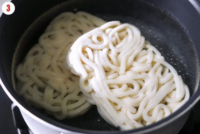 Frozen sanuki udon noodle cakes in a pot of boiled water.