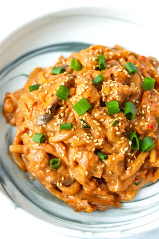 Closeup front view of creamy kimchi udon noodles with blended tofu sauce on a plate.